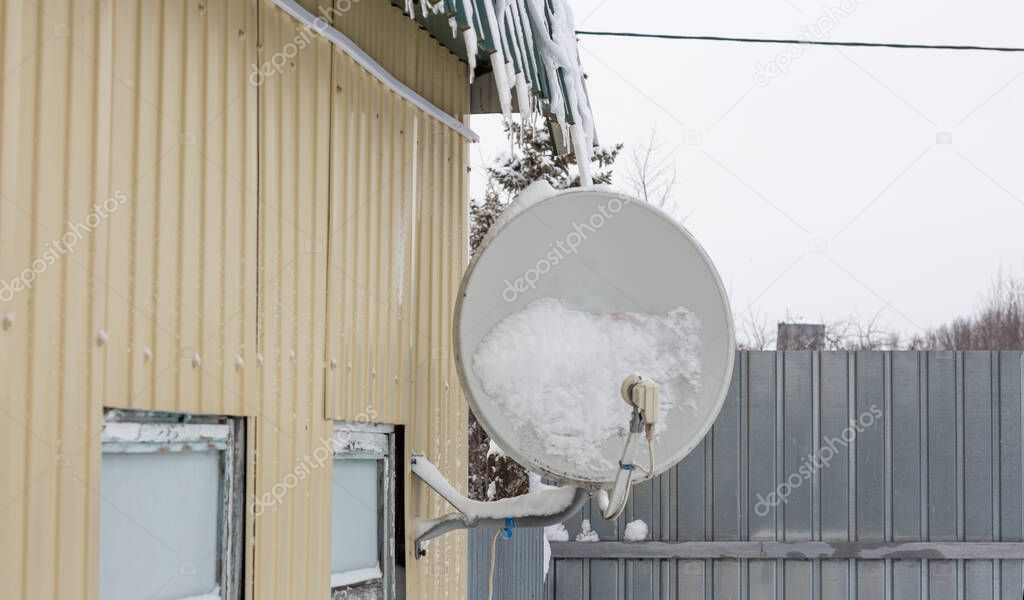 satellite dish fixed to the wall of a house in the snow after a snowfall.