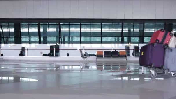 Ung kvinna med ansiktsmask går på flygplatsen terminal driver bagagevagn med många väskor innan incheckning. Koncept för pandemi och resor — Stockvideo