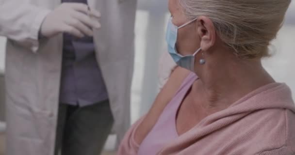 Pacjentka w podeszłym wieku otrzymująca szczepionkę. Pracownik medyczny szczepiący starszego pacjenta przeciwko koronawirusowi, grypie, grypie lub zapaleniu płuc — Wideo stockowe