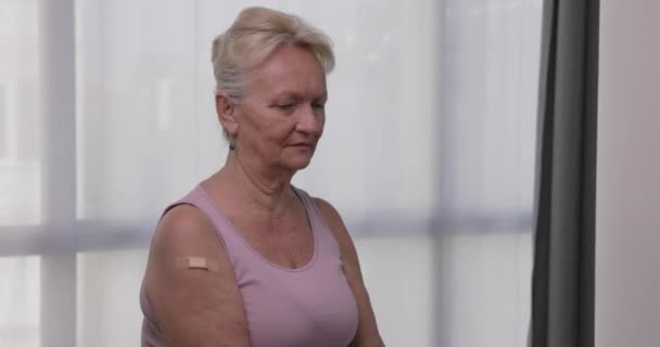 Senior kvinna bär ansiktsmask visar vaccinerad arm med självhäftande plåster och gester tummen upp. Äldre patienter som får vaccination. Koncept för vaccinationsprogram Covid-19 — Stockvideo