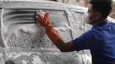 Araba yıkama istasyonunda köpük sabunla araba yıkayan, eldivenli profesyonel bir işçi..