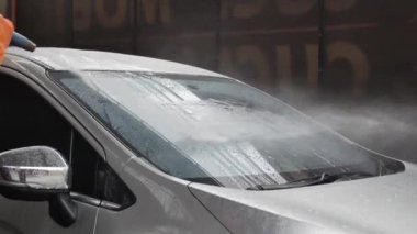 Profesyonel araba yıkama istasyonunda hortumla araba yıkayan profesyonel bir işçi..