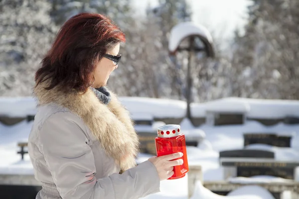 Mid aged woman with candle on snowy cemetery — Stock Photo, Image