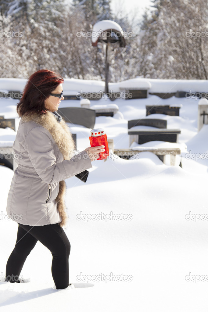 Mid aged woman with candle on snowy cemetery