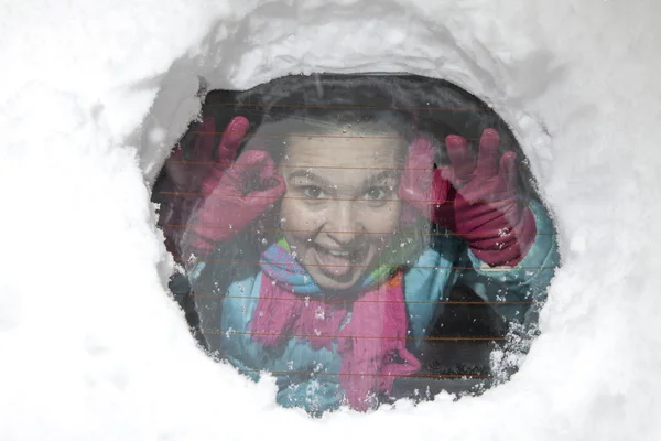 Linda chica sonriente bromeando a través de un agujero en una ventana de coche cubierto de nieve — Foto de Stock