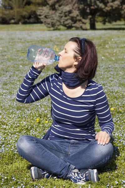 Mulher de meia idade relaxante e água potável na grama — Fotografia de Stock