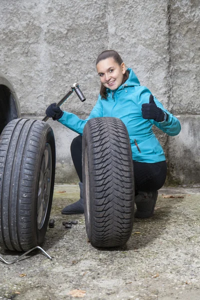 Jovem mulher sorridente motorista substituindo pneus, mostrando sinal OK — Fotografia de Stock