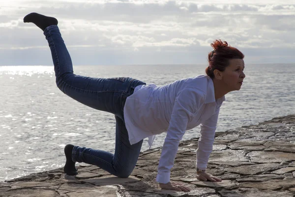 Midden leeftijd vrouw aan de kust uitvoeren van yoga — Stockfoto