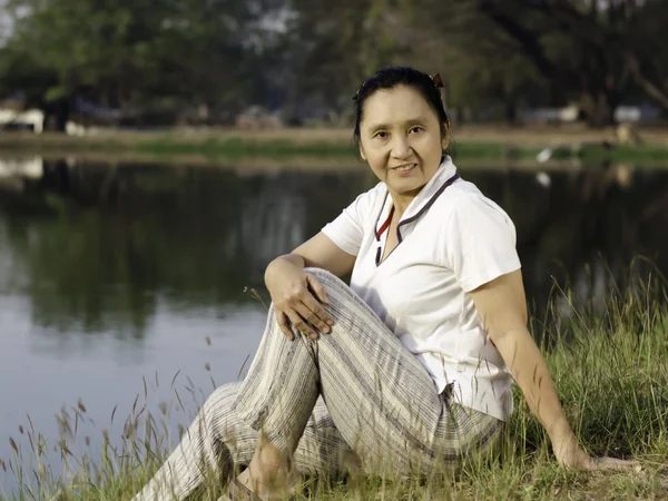 Žena sedí na zelené louce u jezera — Stock fotografie