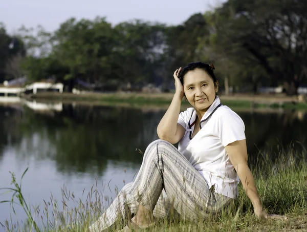 Woman sitting on green field by lake — Stock Photo, Image