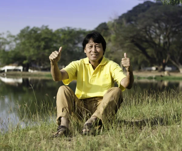 Senior man met duim tegen een groen park — Stockfoto