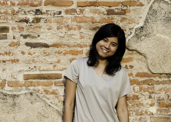 Menina posando e sorrindo enquanto estava perto da parede de tijolo — Fotografia de Stock