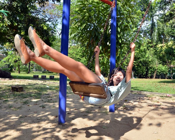 Jovem mulher está balançando em um balanço em um parque — Fotografia de Stock