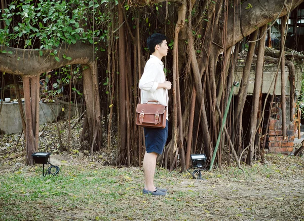 Young man with leather bag, Banyan tree background — Stock Photo, Image