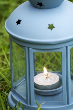 Yeşil çimenlerin üzerinde yanan mum içinde ile mavi fener 