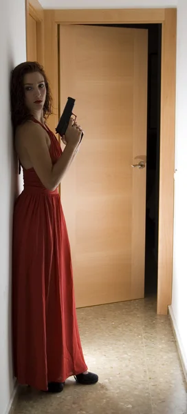 Vacker kvinna med en röd klänning och en pistol — Stockfoto