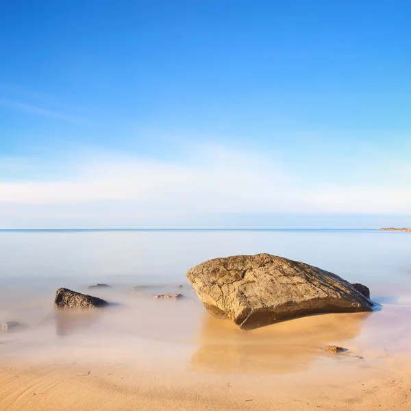 Flat rock on a golden sand beach and sea. Long exposure. — Stock Photo, Image