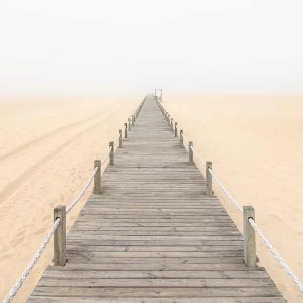 Pasarela de madera sobre un fondo de playa de arena brumosa. Portugal . —  Fotos de Stock