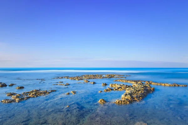 Kameny v modrém oceánu za jasné oblohy na sunrise. — Stock fotografie