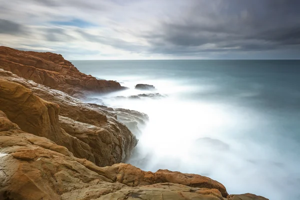 Rochers rouge foncé, mousse et vagues, mer par mauvais temps . — Photo