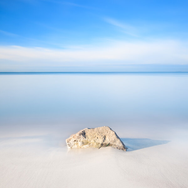 Rock on a white sand beach and sea on horizon.