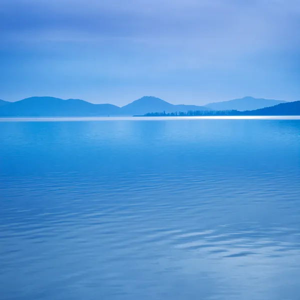 水表面在一个蓝色的早晨在特拉西梅湖，意大利。在背景上的山 — 图库照片