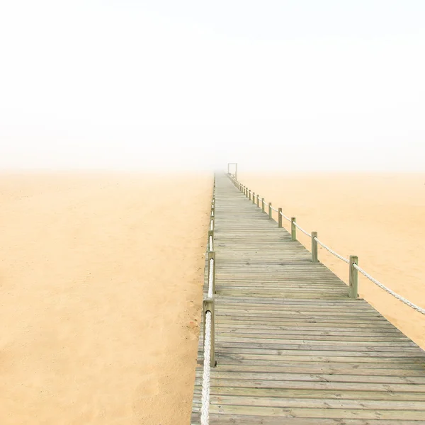 Passarela de madeira em um fundo de praia de areia nebulosa. Portugal . — Fotografia de Stock