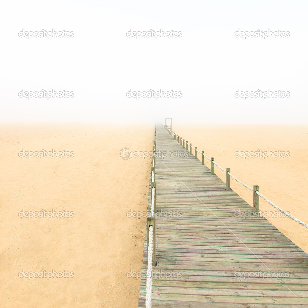 Wooden footbridge on a foggy sand beach background. Portugal.