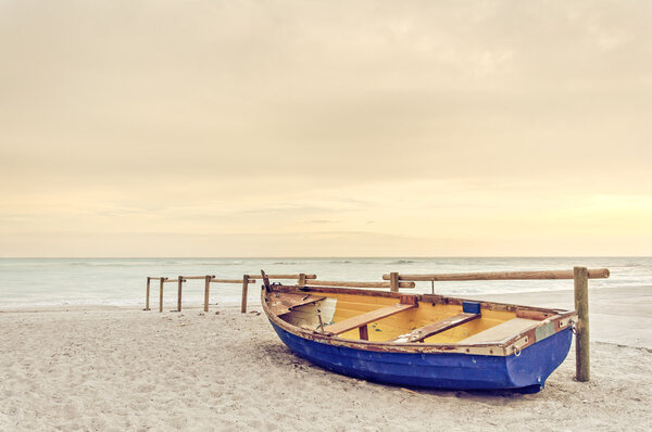 Старая желто-голубая деревянная лодка на белом пляже на теплом закате
