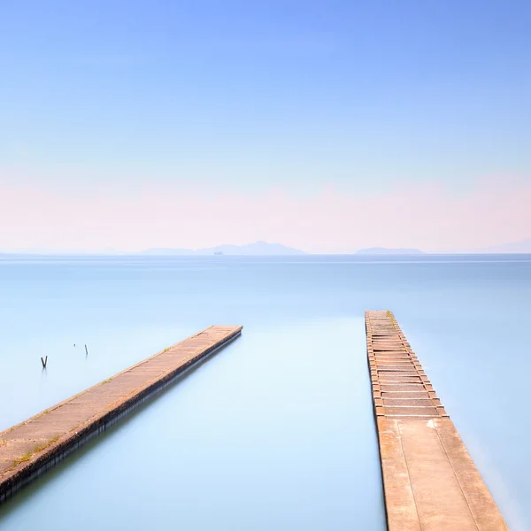 Two concrete pier or jetty on a blue sea. Hills on background — Stock Photo, Image