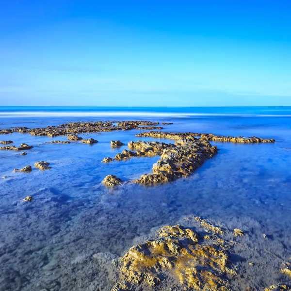 Kameny v modrém oceánu za jasné oblohy na sunrise. — Stock fotografie