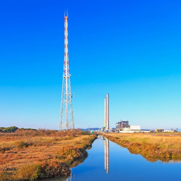 Central elétrica com pilhas de fumaça, torre de transmissão e reflexão sobre a água — Fotografia de Stock
