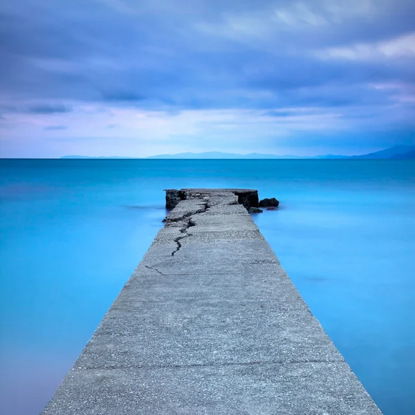 Gebroken beton pier of steiger en stenen op een blauwe zee. heuvels op de achtergrond — Stockfoto