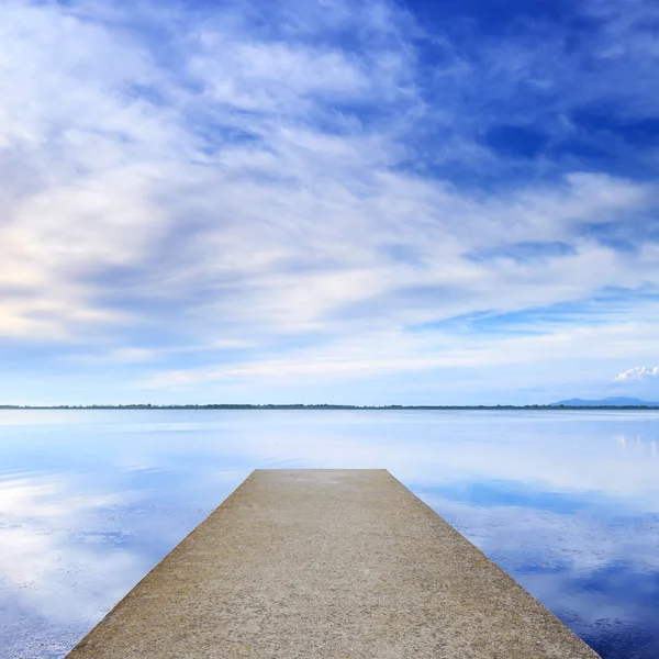 コンクリートの桟橋か突堤と水の上の青い湖と空反射. — ストック写真