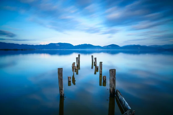 Wooden pier or jetty remains on a blue lake sunset and sky refle — Stock Photo, Image