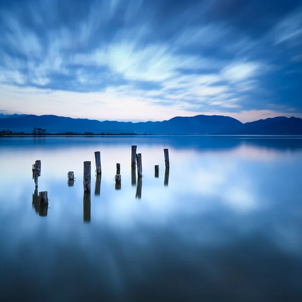 O cais de madeira ou o molhe permanecem em um pôr-do-sol de lago azul e reflexão de céu na água. Versilia Toscana, Itália — Fotografia de Stock