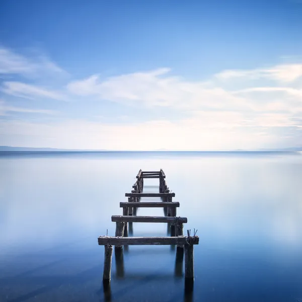 Muelle de madera o embarcadero permanece en un lago azul. Exposición larga . — Foto de Stock