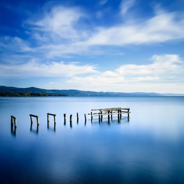 Muelle de madera o embarcadero permanece en un lago azul. Exposición larga . — Foto de Stock