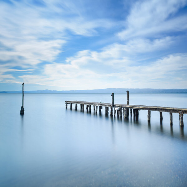 Wooden pier or jetty remains on a blue lake. Long Exposure.