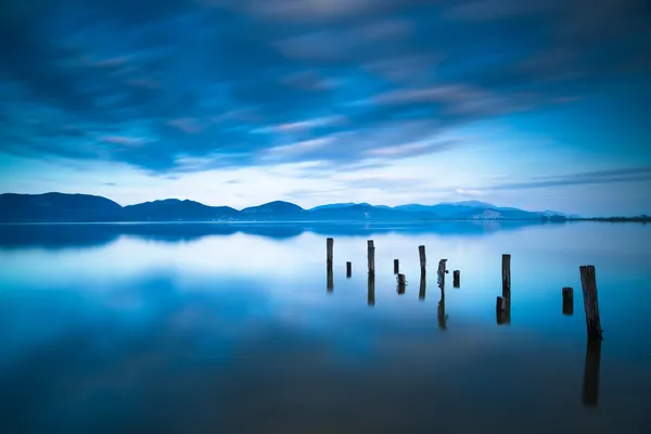 Wooden pier or jetty remains on a blue lake sunset and sky refle — Stock Photo, Image