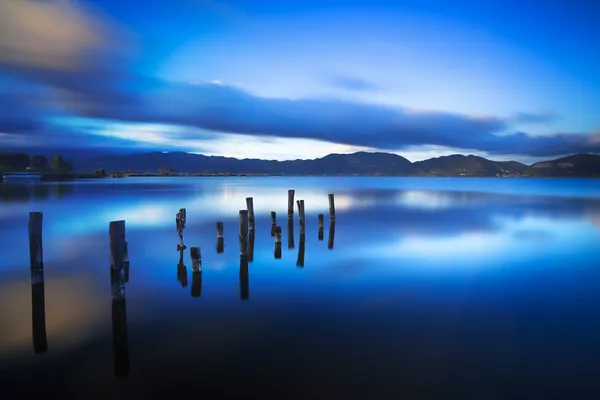 Cais de madeira ou molhe permanece em um pôr do sol lago azul e céu refle — Fotografia de Stock
