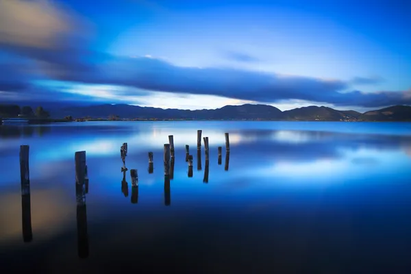 Muelle de madera o embarcadero permanece en un atardecer lago azul y refle cielo —  Fotos de Stock