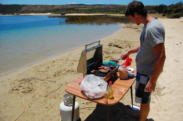 Homme cuisine des saucisses au barbecue à la plage Photos De Stock Libres De Droits