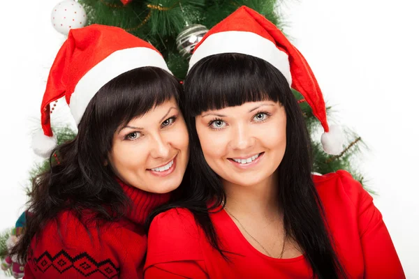 Duas meninas de gorros vermelhos sorriem perto da árvore de Natal — Fotografia de Stock