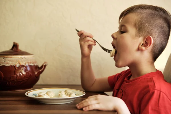 Cute Boy comiendo albóndigas en la mesa en la cocina. — Foto de Stock