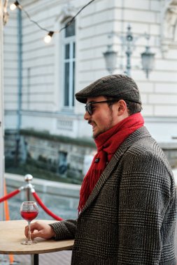 LVIV, UKRAINE - 22 Ekim 2021: Yalnız genç adam Lviv Gıda ve Şarap Festivali 'nin açık hava barında tek başına şarap içiyor. Güneş gözlüğü ve şapkası olan sakallı bir adamın portresi.