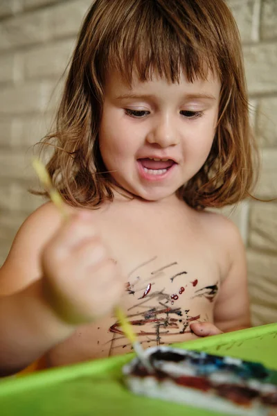 Little girl body painting herself with watercolor paints, having fun with creative playing. Child getting dirty with paints