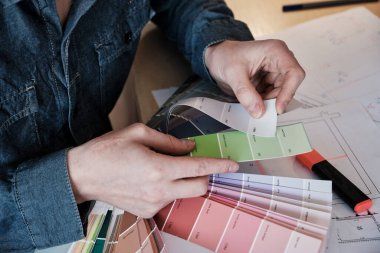 Graphic designer chooses colors from palette guide for painting and printing a new creative business work. Interior designer working in office with color palette.