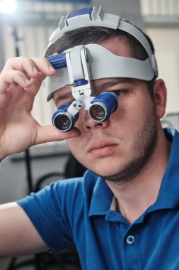 Diş kliniğinde çalışan dürbün büyüteç takan bir diş hekimi. Protez ve implantoloji kavramı.