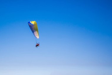 Açık mavi gökyüzünün altında bir paraglider uçuran adam